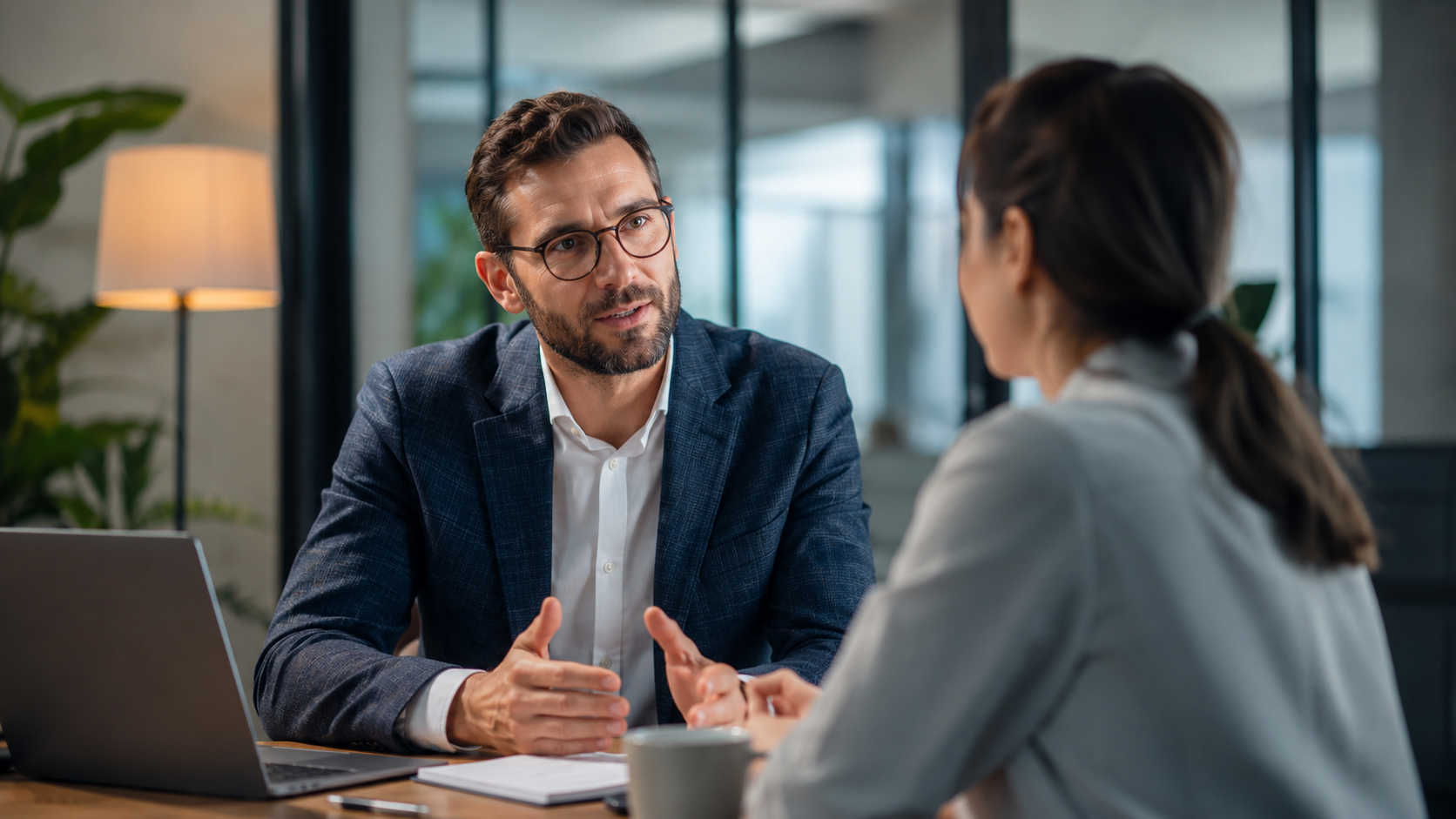 Conversación de feedback y coaching entre un líder y una colaboradora en una sala corporativa.